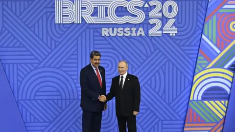 Getty Images Venezuela's President Nicolás Maduro shakes hands with his Russian counterpart, Vladimir Putin, in front of a sign promoting the 2024 Brics summit in Kazan