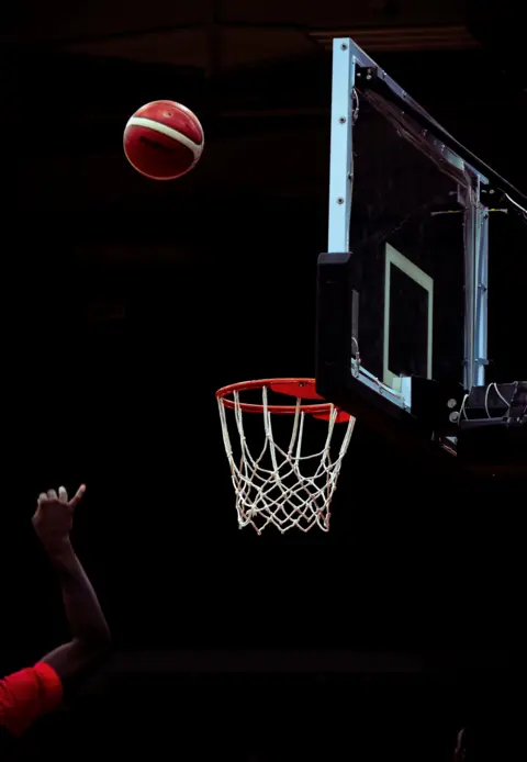 Matt Kirk Red and white ball thrown mid air, aiming to go in a basket ball hoop 