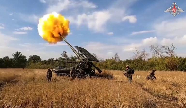 Russian soldiers stand watching as a talk fires into Ukrainian positions