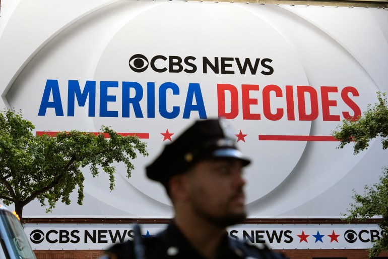 A police officer stands in front of a sign advertising the CBS News "America Decides" vice presidential debate.