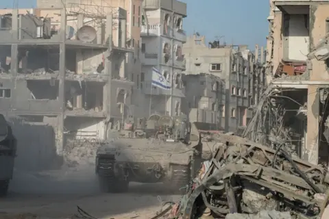 Getty Israeli troops and an armoured personnel carrier patrol through the streets of a rubble-strewn Rafah in September 2024