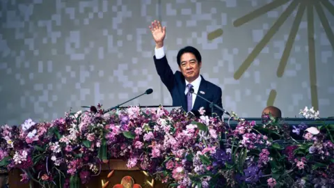 Getty Images William Lai, in a suit, waves an arm towards the crowd while on stage