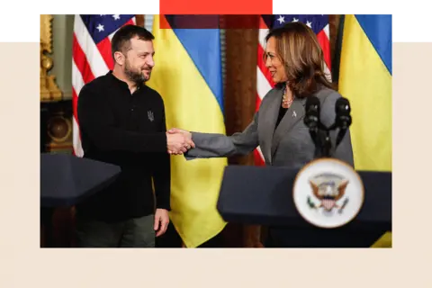 Volodymyr Zelensky and Kamala Harris shake hands on a stage in front of the Ukrainian flag and the US flag