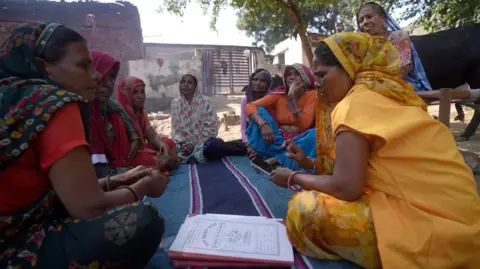 Saraskanth TK A group of women sitting together on the ground as one of them uses her phone in India's Haryana state