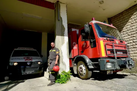 Darren Conway / BBC Samir El Chekieh standing next to fire engine and an ambulance.