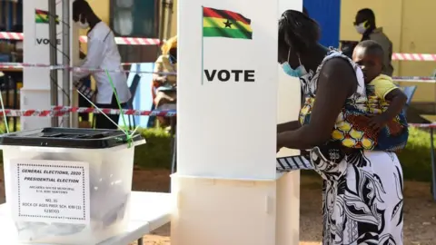 AFP A woman with a baby tied to her back stands at an outdoor polling booth to mark her ballot paper.