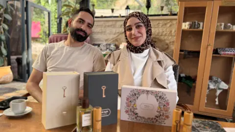 Sebastian Usher Qassem Abu Khalaf and his wife Malak Hijaz with a range of their perfumes on a wooden table.