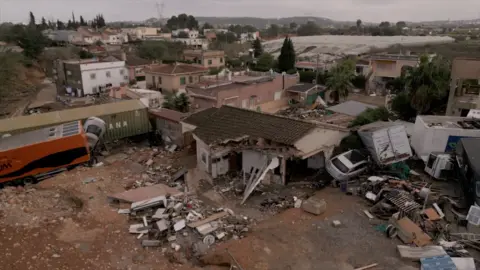 The Matías family home is partially collapsed. Some of the roof has caved in and some walls are missing. It is surrounded by debris and rubble, as well as cars and lorries