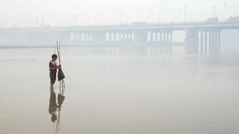 Reuters Young boy is setting up a fishing trap, with the bridge over the River Ravi in the background, amid smog in Lahore