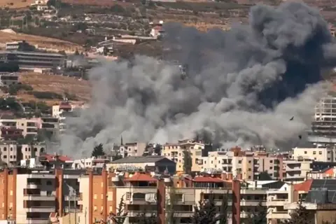 Smoke rises from buildings on fire hit by a missile strike.