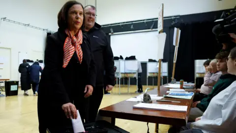 Reuters Mary Lou McDonald casting her vote. She has shoulder length brown hair and is wearing a orange and white scarf.