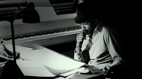 Netflix Quincy Jones in the recording studio, wearing a black hat and polo shirt