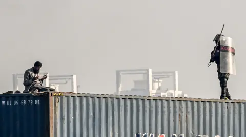 AFP A man is seen praying on top of a shipping container as a paramilitary soldier approaches him during a protest demanding the release of former prime minister Imran Khan, at the Red Zone area in Islamabad on November 26, 2024. 