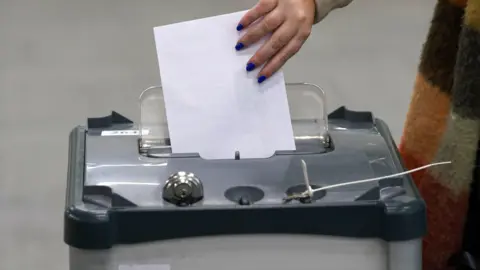 PA Media A woman places a white ballot in a grey vote box.