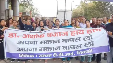 AK Mishra Protesting residents seen holding a banner that calls for Dr Ashok Bajaj to revoke the sale of his house