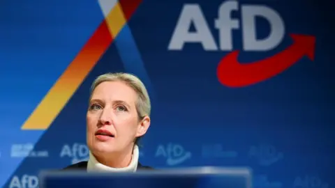 Reuters Alice Weidel of Germany's far-right AfD sits behind a lectern at a party conference, with the name of the party emblazoned on the wall behind her