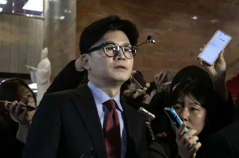 Getty Images Han Dong-hoon surrounded by reporters as leaves the party's meeting at the National Assembly in Seoul