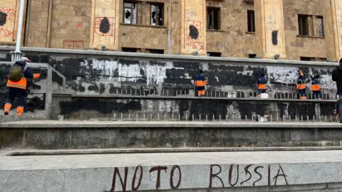 Cleaners remove graffiti from the walls outside parliament in Georgia