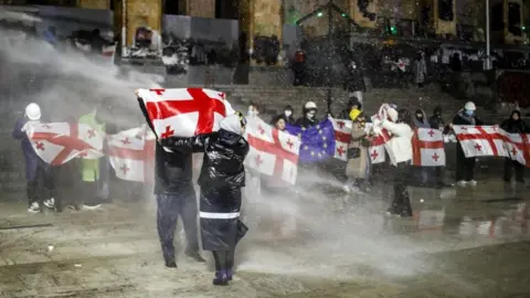 EPA-EFE/REX/Shutterstock Protesters holding Georgian flags are doused with water cannon outside the Georgian parliament