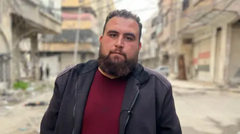 Aamir Peerzada/BBC A man standing in the middle of a street, looking straight into the camera