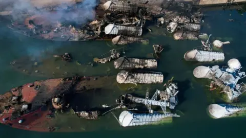 Getty Images An aerial photo of multiple sunken ships next to the dockside. Smoke is rising.