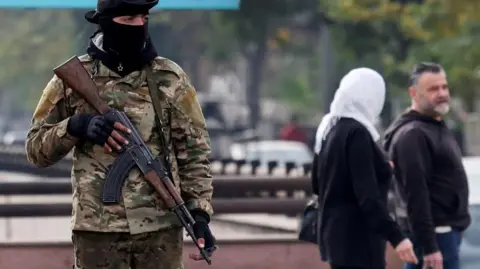 Reuters man in camouflage with a gun stands in Damascus as a couple walk past in the background