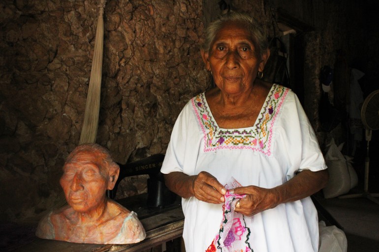 Catalina Kankub Hab, 85, a seamstress from Dzan, Yucatán, Mexico, stands next to her self-sculpture made by Luis May Ku, 49, and adorned with Maya Blue paint inside her home on 9 September, 2024