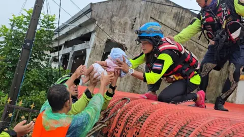 Reuters Rescuers on top of a roof, passing down a baby to other rescuers on a boat in floodwater