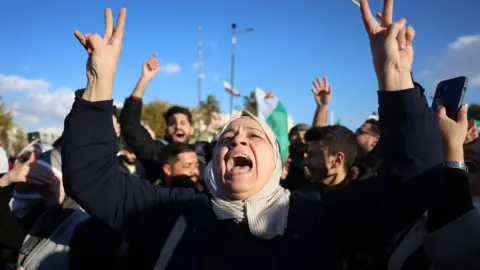 EPA A Syrian woman, with both arms raised, shouting in celebration, in a big crowd