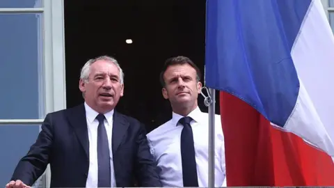 Getty Images François Bayrou, wearing a suit and tie, stands next to France's president Emmanuel Macron, alongside a French flag