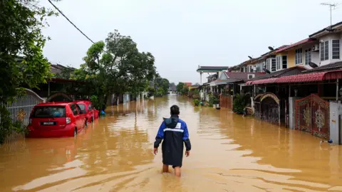 EPA A person standing in the middle of a flooded street, where water is hitting them at knee-level