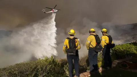 Getty Images Monterey County Firefighters watch as a LA County helicopter comes in to make a water drop on the Palisade Fire