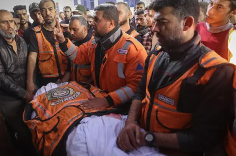 AFP Members of the Gaza Civil Defence attend the funeral of a colleague who was killed alongside his son in an Israeli strike in Gaza City.