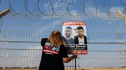 Reuters Israeli woman holds poster of Israeli hostages while looking through fence towards Gaza (file photo)