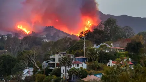 Getty Images A wildfire burns on a hill with buildings below.