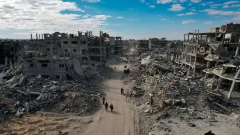 EPA An aerial view taken with a drone shows internally displaced Palestinians walking along a street among the grey, dusty rubble of destroyed buildings in Rafah 