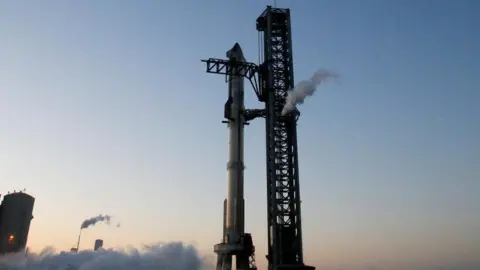 Reuters SpaceX's Starship rocket stands vertically on a launchpad, with a clear blue sky in the background
