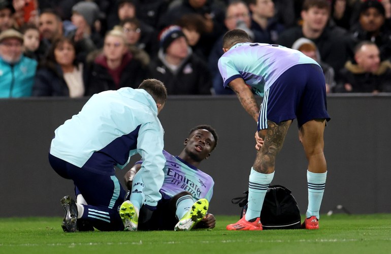 LONDON, ENGLAND - DECEMBER 21: Bukayo Saka of Arsenal reacts as he receives medical treatment after picking up an injury whilst speaking with Gabriel Jesus during the Premier League match between Crystal Palace FC and Arsenal FC at Selhurst Park on December 21, 2024 in London, England. (Photo by Alex Pantling/Getty Images)