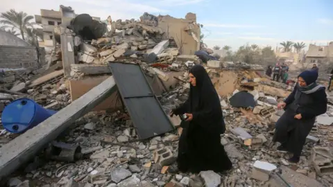 Getty Images Two Palestinian women search and collect usable items among the rubble of a completely destroyed house in Gaza.