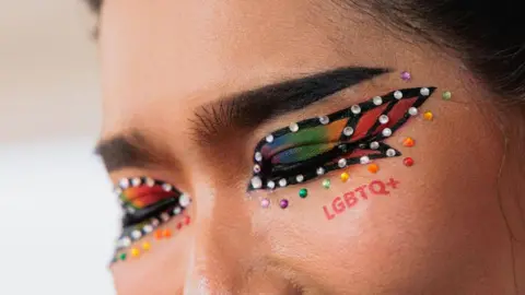 Getty Images A woman with her face painted and rainbow-coloured eye shadow sports the letters LGBTQ+ in red below her closed eyes. The photo was taken in 2024 during the Pattaya Community Pride Parade in Thailand.