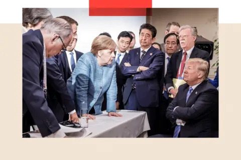 Getty Images Former German Chancellor Angela Merkel deliberates with Donald Trump during the G7 summit, as he sit with his arms folded