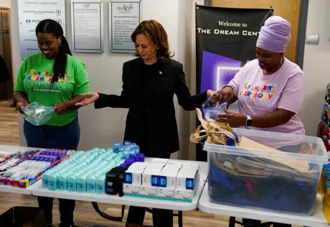 Reuters Kamala Harris flanked by emergency aid workers looking at essential supplies laid out on tables in North Carolina