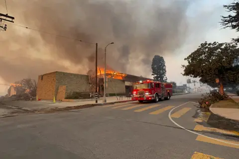 Bellocqimages/Bauer-Griffin/GC Images A fire engine drives down Sunset Boulevard as a building butns in the background with smoke rising on Wednesday