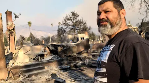 Hipolito Cisneros stands in front of the ashes of his home in Altadena, California