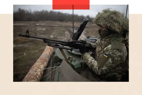 Getty Images A close-up of a Ukrainian soldier inside a tank, holding a rifle at the ready